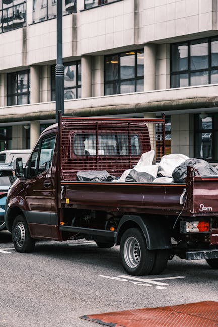 A collection of overflowing waste bins and a large pile of assorted rubbish including cardboard boxes, paper bags, plastic and paper packaging, black garbage bags, and discarded packaging material, si